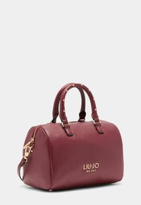 Burgunderfarbenes, strukturiertes Leder-Handtasche mit goldfarbenen Beschlägen, doppelten Griffen und Logodetail auf der Vorderseite. Reißverschluss oben.