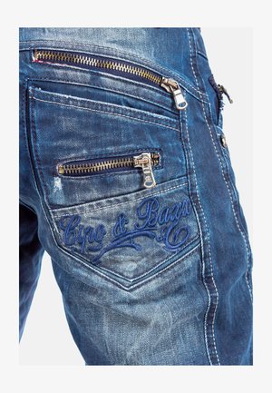 Dunkelblaue Denim-Jeans mit mehreren Reißverschlusstaschen, goldenen Beschlägen und gesticktem Logo-Detail auf der Gesäßtasche.