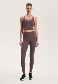 Športový crop top a legíny z tlmeného mauve materiálu; priliehavý strih, hladká textúra a vysoký pás. Čierne tenisky s bielymi podrážkami.