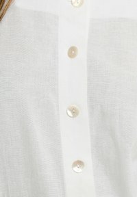 Camicia bianca di lino con chiusura a bottoni. Presenta grandi bottoni chiari e un tessuto leggermente strutturato.