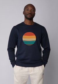 Navy Sweatshirt mit einem runden Grafikdesign, das horizontale Streifen in Orange, Gelb und Türkis zeigt. Aus weichem Stoff und mit Rundhalsausschnitt.