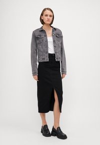 Veste en denim grise délavée, design ajusté, avec deux poches poitrine. Jupe midi noire avec une fente à l'avant. Chaussures plates-formes noires robustes.