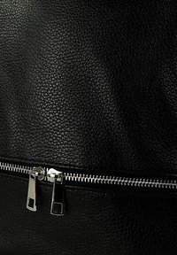 Sac en cuir noir texturé avec une fermeture éclair argentée dotée de deux tirettes métalliques et d'une zone d'accent lisse au-dessus de la fermeture.