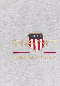 Grauer Sweatshirt mit gesticktem Wappenschild-Logo, roten und weißen Streifen, goldener Schrift "GANT" und "AMERICAN SPORTSWEAR" sowie dem Jahr "1949."