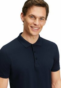 Granatowa koszulka polo wykonana z miękkiego materiału, z klasycznym kołnierzykiem, zapięciem na trzy guziki i krótkimi rękawami w dopasowanym kroju.