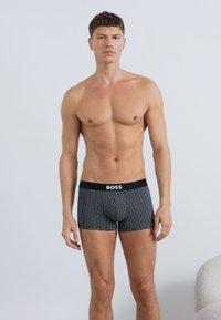 Fekete férfi boxeralsó geometrikus mintával, rugalmas anyagból készült. Egyszínű fekete derékrésszel, amelyen a "BOSS" logó látható.