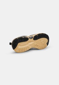 Suola di scarpa sportiva in nero e crema. Presenta una gomma testurizzata per una presa sicura, un design stampato e un'etichetta sul retro per una facile indossazione.