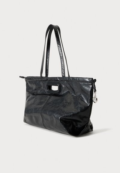 Sac à épaule en cuir noir brillant avec doubles sangles, poignée découpée rectangulaire et petit charme en forme de cœur sur la tirette de fermeture éclair latérale.