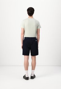 Lys grønn, T-skjorte med kort erm kombinert med marineblå shorts med elastisk midje og lommer. Modell som har på seg hvite sokker og svarte sko.