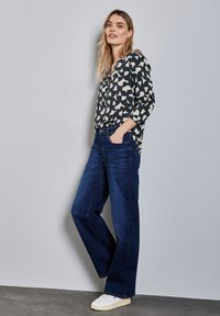 Blusa a righe in bianco e nero abbinata a jeans a gamba larga blu scuro e sneakers bianche; tessuto morbido e design casual.