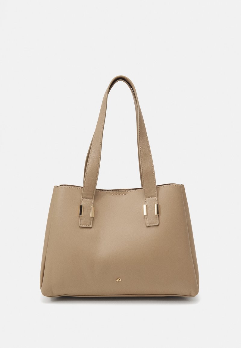 Sac cabas couleur taupe avec deux bretelles et des accents métalliques dorés, avec un petit logo doré près du bas au centre.