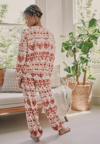 Rot-weißes Schlafanzugset mit Herz- und geometrischen Mustern, aus weichem Material gefertigt. Das Outfit hat lange Ärmel und eine lockere Passform bei den Hosen.