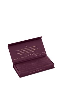 Una scatola viola scuro si apre per rivelare una maschera per gli occhi in seta, foderata con testo dorato e accenti a forma di stella. La maschera è delicatamente piegata all'interno per essere riposta.