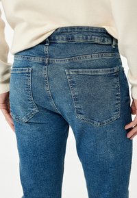 Jeans de mezclilla azul con una textura suave, de cintura alta y dos bolsillos traseros. Presentan un corte clásico y costuras reforzadas.