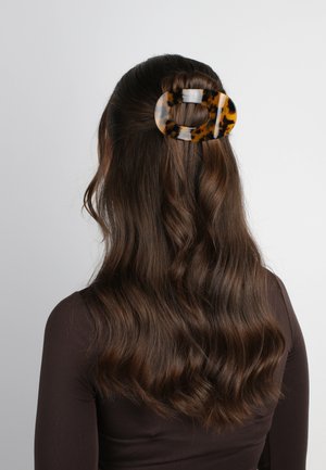 Grande forcina per capelli in tartaruga, realizzata in plastica lucida. Forma ovale con una finitura lucida, che tiene ferme le onde dei capelli castani dietro.