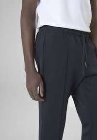 Marineblauwe sweatpants van zachte stof, met een elastische tailleband met trekkoord, zijzakken en een getailleerde pasvorm.