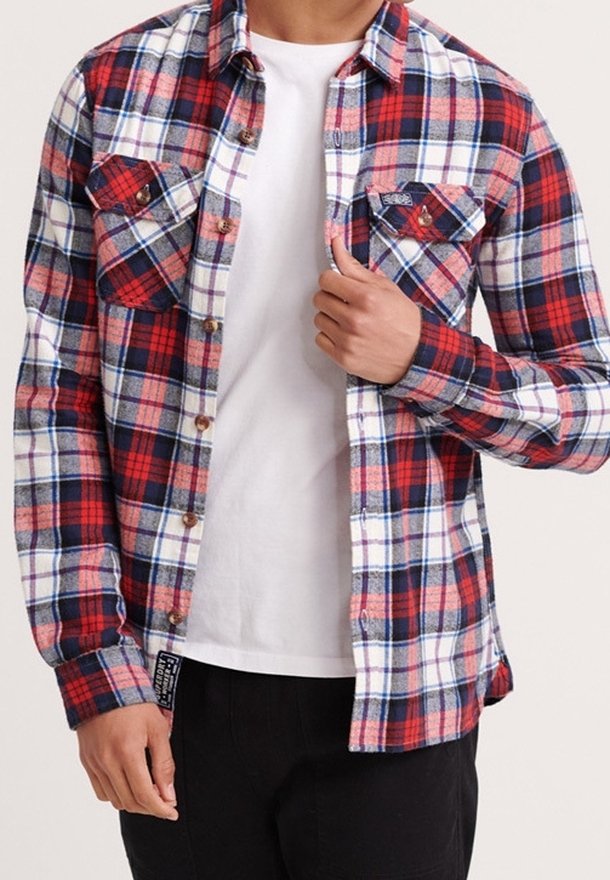 Rød, hvid og blå ternet flannelskjorte med to brystlommer, knapper ned foran og en lige kant. Båret over en hvid T-shirt.