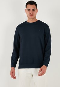 Felpa blu navy realizzata in tessuto morbido, con colletto a girocollo, maniche lunghe e un piccolo logo sul petto. Texture liscia e vestibilità comoda.