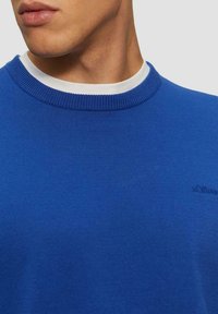Blauer Pullover mit rundem Halsauschnitt, geripptem Textur und weißem Innenkragen. Verfügt über dezente Markenkennzeichnung auf der Brust.