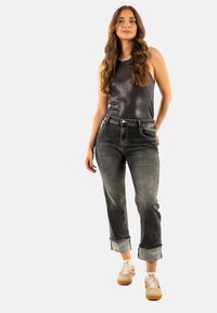 Top nero senza maniche con una finitura lucida, abbinato a jeans in denim grigi. I jeans hanno orli arrotolati e una texture sbiadita.