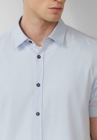 Himmelblaues kurzärmliges Hemd aus strukturiertem Stoff mit Kragen, das kontrastierende dunkle Knöpfe entlang der Knopfleiste aufweist.