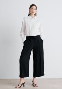 Λευκό πουκάμισο με κουμπιά, μαύρο φαρδύ παντελόνι με ζώνη στη μέση και μαύρες ψηλές σαμπφόρτες. Λείο ύφασμα, χαλαρή εφαρμογή, casual στυλ.