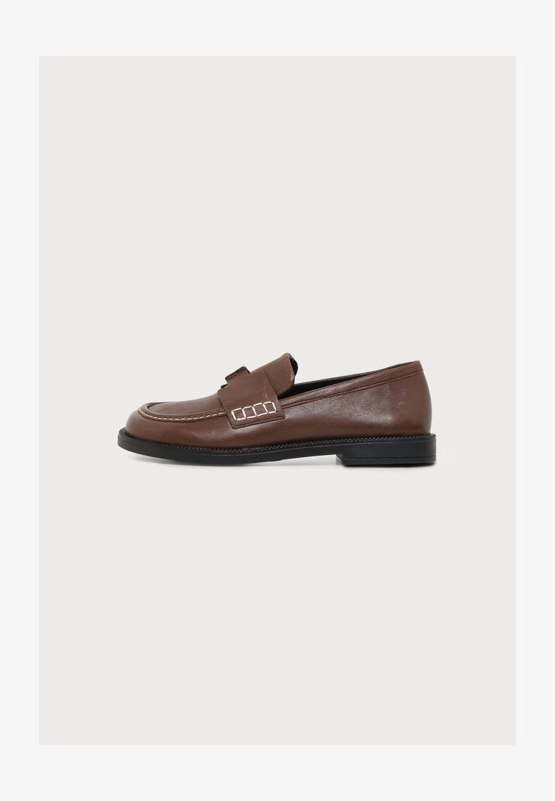 Mocassin en cuir marron avec semelle noire et détail de couture décorative près de la bride, vu de côté sur fond blanc.