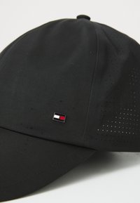 Black cap made of textured fabric, featuring a curved brim and vented paneling. Small logo accent in red and white on the front.