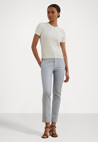Cream knitted short-sleeve sweater with cable knit pattern, paired with light blue fitted pants and brown heeled sandals.