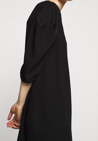 Svart klänning med rund halsringning, 3/4-puffärmar och löst sittande passform. Mjuk textur och minimalistisk design utan synliga mönster eller hårdvara.
