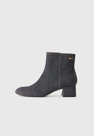 Bottine en denim foncé avec un bout pointu, un talon bloc, des coutures visibles et un logo de marque subtil sur le côté. Texture lisse.