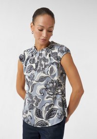 Blumenbluse aus hellblauem Satinstoff mit gerafftem Ausschnitt, kurzen Ärmeln und aufwendigen schwarz-weißen Blumenmustern.