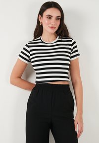 Mustriga must-valge lühikeste varrukatega crop-top, ümmargune kaelus ja keha lähedal lõige, koos kõrge vöökohtadega mustade pükstega.