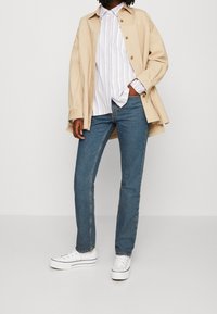 Giacca camicia oversize beige, camicia button-up a righe bianche e pastello, jeans blu a gamba dritta e sneakers platform bianche.