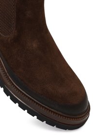 Bruine suède enkelboot met elastische zijkanten, ronde neus en een gestructureerde rubberen zool. Heeft een gestikte leren bies.