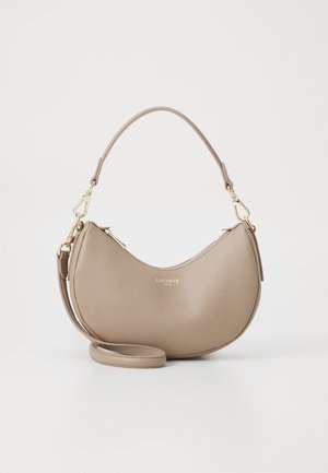 Borsa a mano in pelle beige a forma di mezzaluna con zip superiore, tracolla staccabile e logo dorato "Lacoste Paris" sul davanti.