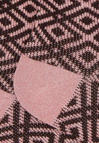 Nahaufnahme von gestricktem Stoff mit geometrischem Muster in Pink und Dunkelbraun, das ein mit mir gesticktes pinkes Patch in Form eines Handschuhs zeigt.