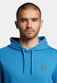 Felpa blu realizzata in misto cotone con tasca frontale e cappuccio con cordino. Presenta un piccolo logo giallo ricamato sul petto.