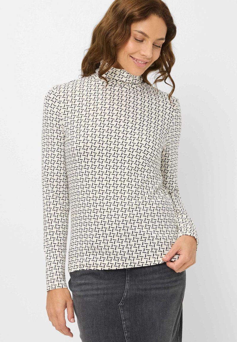 Langærmet turtleneck-top i creme med sort geometrisk mønster, med en tætsiddende silhuet og blødt, strækbart stof. Glat tekstur.