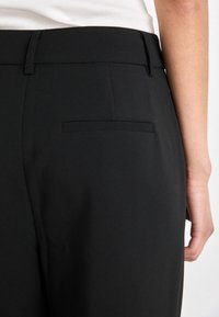 Svarta skräddarsydda byxor med en slät textur, med en bakficka som har en diskret söm. Midjan är platt, designad för en figurnära look.