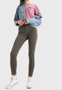 Jeansjacka över en röd randig t-shirt, kombinerat med olivgröna tajta jeans och vita höga sneakers. Enkel avslappnad outfit.