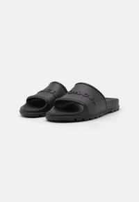 Black rubber slide sandals with open toe, rounded shape, embossed logo on strap, textured sole, and minimalistic design.