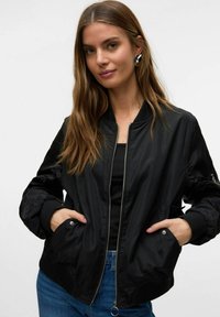 Veste bomber noire avec fermeture éclair à l'avant, poignets côtelés, deux poches latérales et un design épuré. Tissu lisse et brillant avec une coupe décontractée.