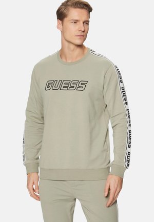 Felpa verde chiaro con un grande logo nero "GUESS" sul davanti e strisce nere decorative lungo le maniche con branding ripetuto.