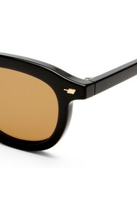 Μαύρα ορθογώνια γυαλιά ηλίου με καφέ φακούς και ένα μικρό χρυσό λογότυπο στην πάνω γωνία του αριστερού σκελετού.
