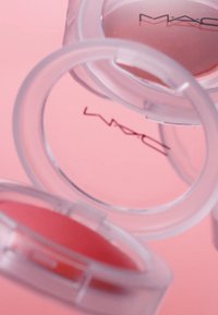 Compact de fard à joues MAC dans des boîtiers en plastique transparent, présentant une texture poudreuse rose douce et le logo MAC en noir sur la surface intérieure.