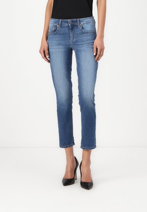 Jeans in denim blu chiaro con una vestibilità slim, lunghezza cropped, cinque tasche e un orlo leggermente sfilacciato, abbinati a scarpe con tacco alto nere.