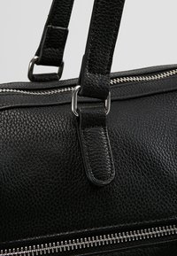 Czarna skórzana torebka o teksturowanej powierzchni, z srebrnymi metalowymi elementami i regulowanymi paskami. Charakteryzuje się wyraźnym suwakiem wzdłuż dolnej krawędzi.