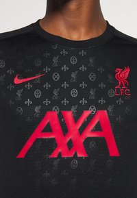 Černé sportovní tričko z látky s texturovaným vzorem log, červeným znakem Nike, vyšívaným červeným erbem Liverpoolu a velkým červeným nápisem "AXA".