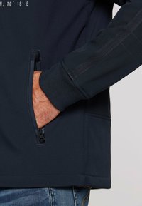 Marineblaues Jacket mit seitlichen Reißverschlusstaschen, gerippten Bündchen und einer glatten Textur. Verfügt über einen grafischen Aufdruck auf der oberen Vorderseite, der das Design verbessert.
